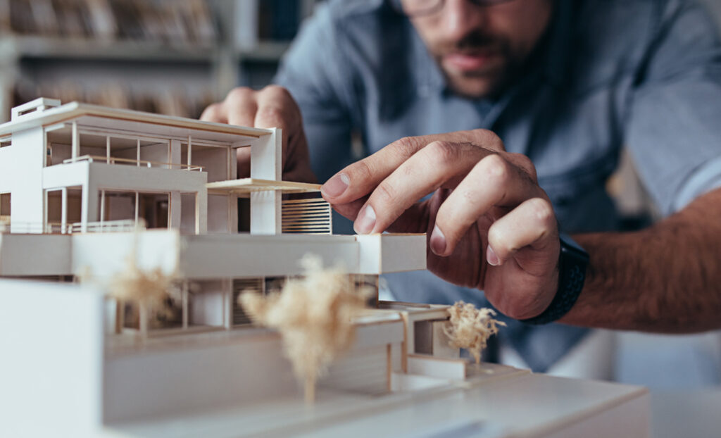 Close up of male architect hands making model house Man architect working in the office