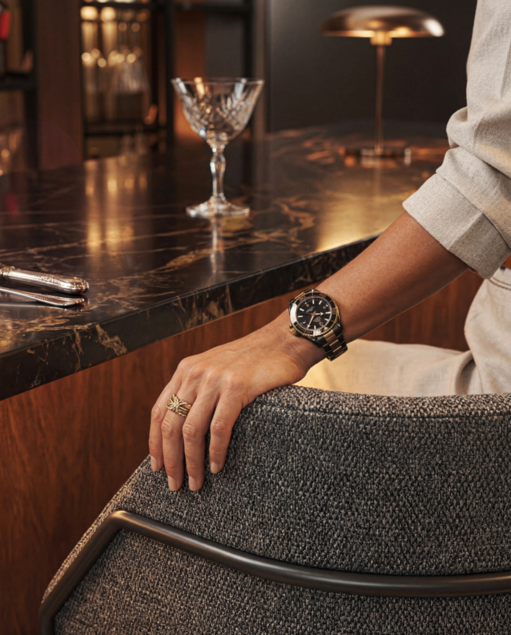 The hand of a person with a tasteful wristwatch lingers on the back of a fibreguard fabric chair in a chic modern dining setting